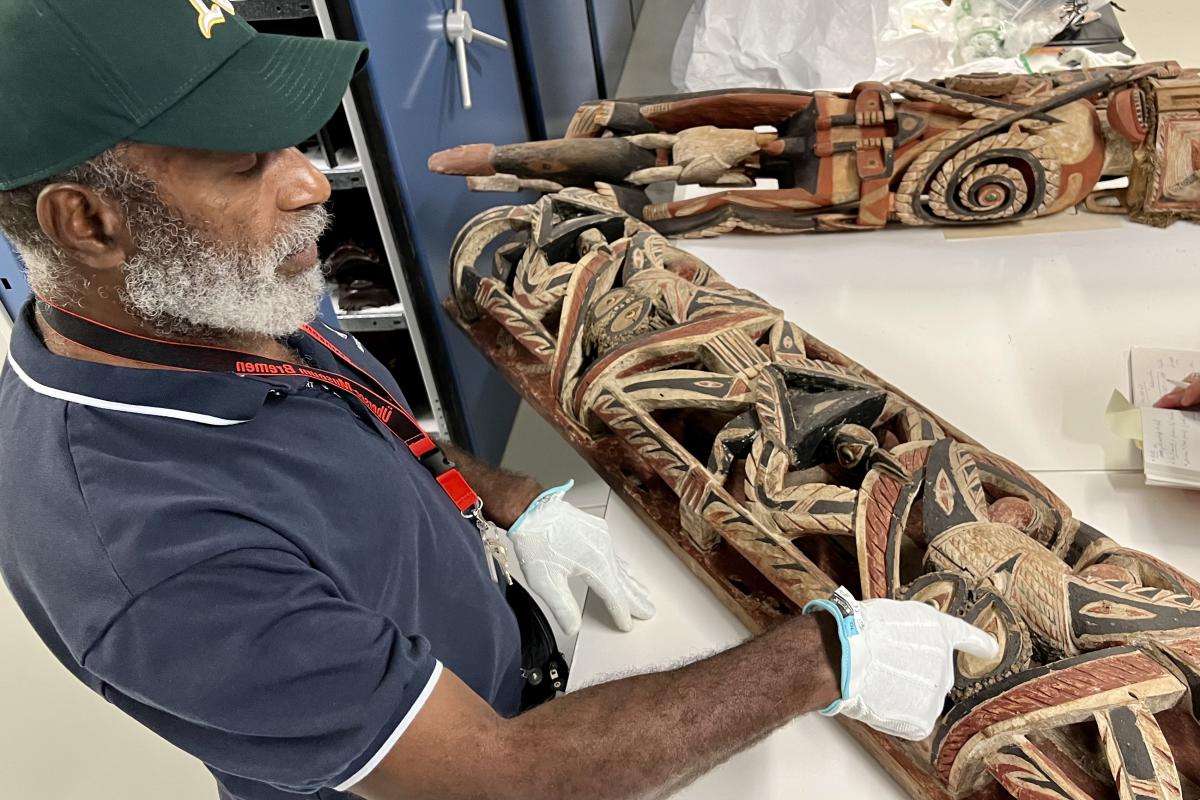 Papua New Guinean carver looks at wooden artwork.